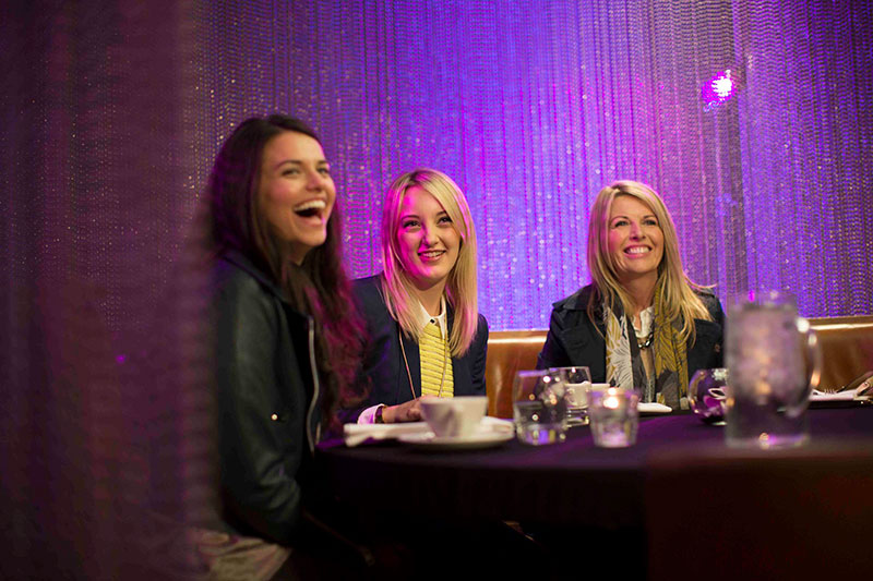 Three women smiling and laughing in a private booth surrounded by hanging gems
