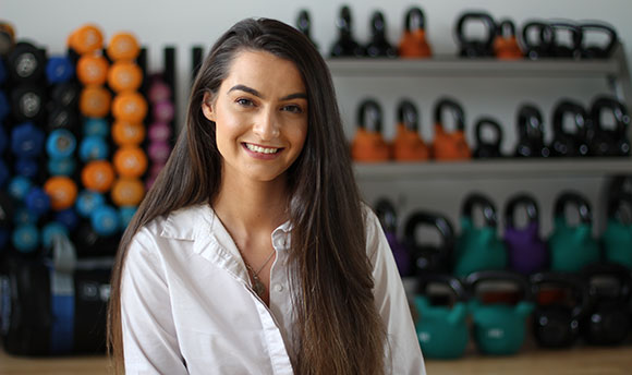 A young brunette woman in a gym beside the kettlebells and weights