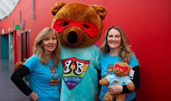 Two smiling women next to someone in a large bear costume